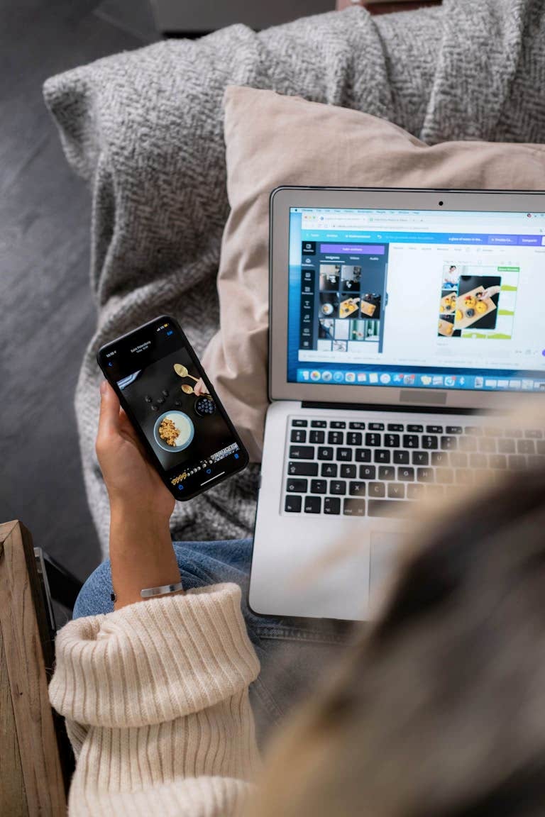 A woman multitasks, using a laptop and smartphone for design work, sitting on a sofa indoors. Ankara web tasarım, seo ajansı