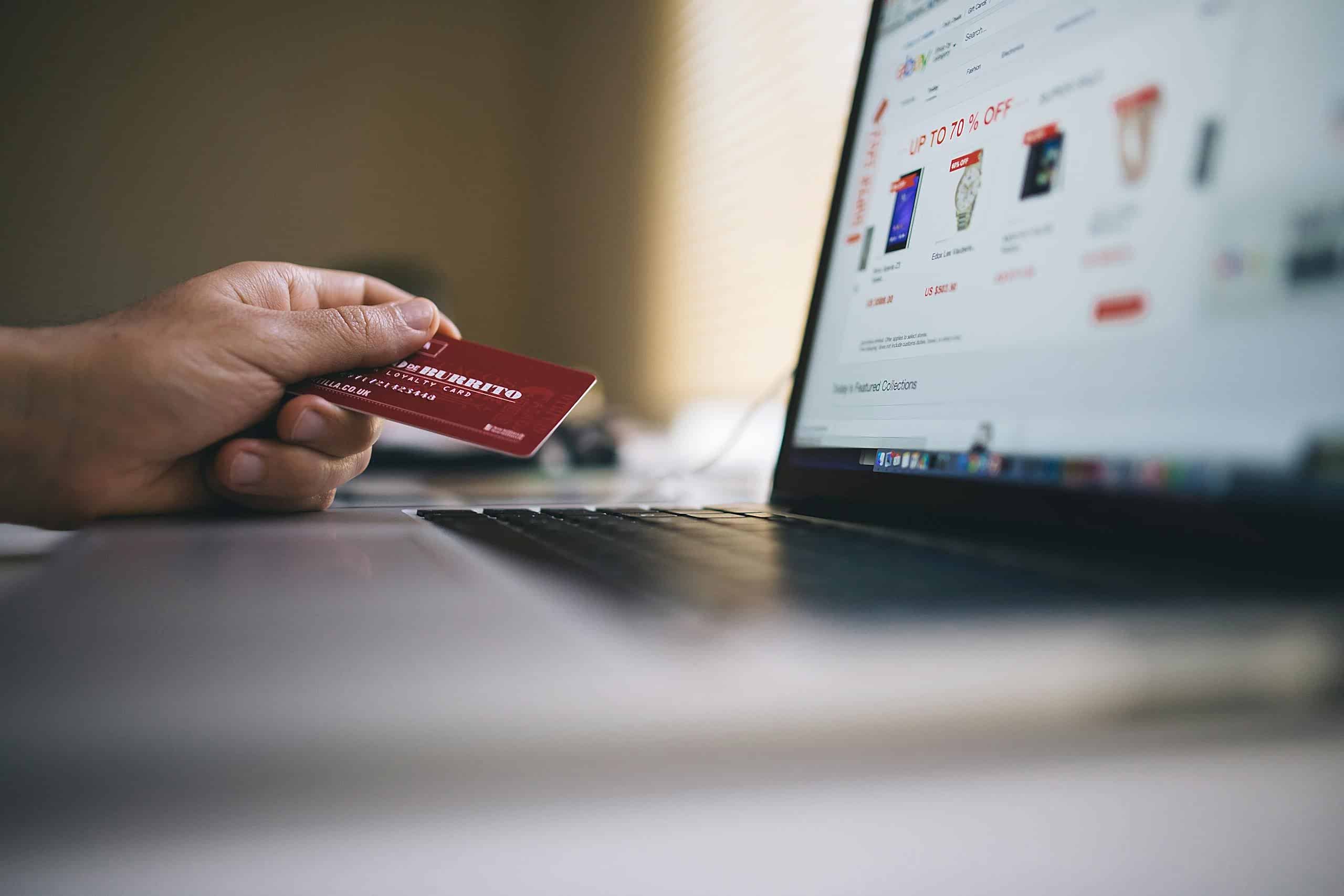 Person holding a credit card while shopping online on a laptop, indicating ecommerce transactions. ankara e-ticaret web sitesi yapimi ve paketleri